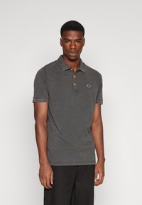 Polo gris de manga corta, con una tapeta de tres botones en naranja, costuras en contraste y un pequeño logotipo bordado en el pecho.