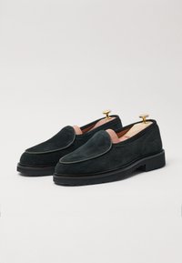 Black suede loafers with a rounded shape, contrasting stitching, and gold heel taps. The design features a smooth inner lining and subtle detailing.