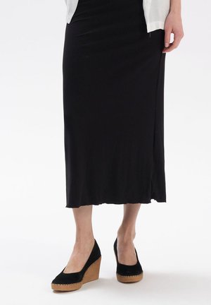 Czarna midi spódnica ze żłobieniami połączona z czarnymi bucikami na platformie, które mają teksturowaną czarną cholewkę i brązową, plecioną platformę. Prostota i elegancja formy.