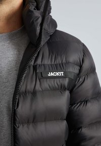 Herre sort dunjakke med høj krave, lynlås foran og en glat tekstur. Har et mærketiket "JACKIT" på brystet.