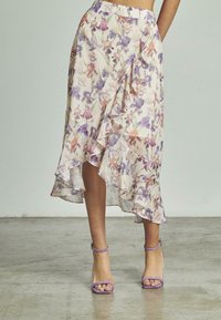 Jupe midi à motifs floraux avec un ourlet à volants, présentant des motifs violets, roses et beiges sur un tissu léger. Associée à des escarpins à bride de cheville violets.