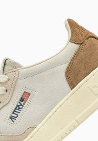 Sneaker con tomaia in suede beige, con un tassello sul tallone in suede marrone, intersuola bianca e una patch etichettata con un design della bandiera americana.