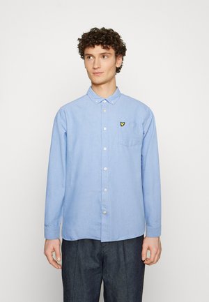 Camicia button-up azzurro chiaro realizzata in tessuto intrecciato, con taschino e un piccolo emblema di farfalla gialla sul lato sinistro del petto.