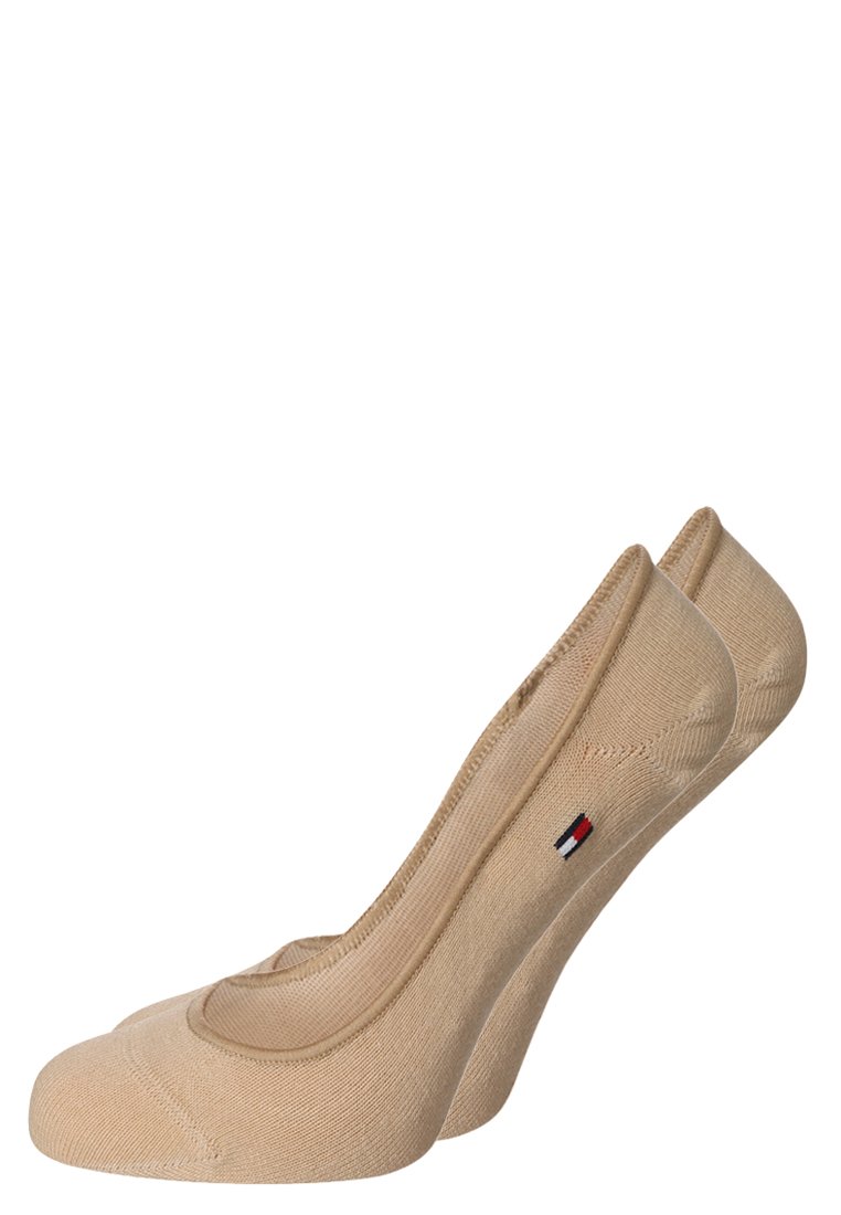 Calcetines tobilleros beige con un diseño curvo, textura suave y un pequeño acento de logo en rojo, blanco y azul cerca del puño.