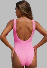 Rosa stickad baddräkt med djup rygg, breda axelremmar och vågiga kanter, som visar en texturerad yta.