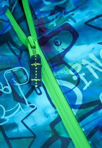 Blå och grön zippered tyg med abstrakta mönster. Tjock grön dragkedja och ett marinblått drag med gula accenter. Slät textur.