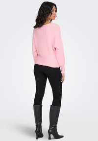 Maglione rosa a costine, dalla vestibilità ampia, con scollo rotondo, indossato con jeans skinny neri e stivali neri alti fino al ginocchio con tacco. Vista posteriore del completo.