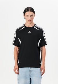 T-shirt de sport noir à manches courtes, avec des accents blancs et le logo Adidas sur la poitrine. Présente une coupe décontractée et un design contrastant au niveau des épaules.