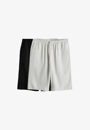 Kaksi paria joustovyötäröisiä shortseja, yksi valkoinen edessä nyörillä ja yksi musta, aseteltuna tasaisesti valkoista taustaa vasten.