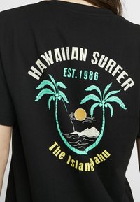 Černé bavlněné tričko s barevným grafickým motivem palmových stromů, slunce a surfovací scény, s nápisem "HAWAIIAN SURFER EST. 1986" a "The Islandahu" níže.