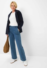 Mørk navy jakke, hvid T-shirt og brede blå denim jeans, parret med hvide sneakers og en brun ruskinds taske med nitter.