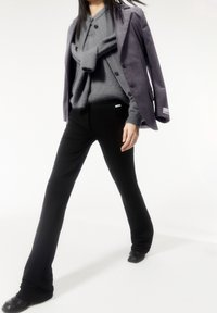 Šedý přizpůsobený blazer přes šedý pletený svetr, s černými kalhotami rovného střihu a černými botami. Hladké textury a přiléhavý design.