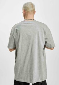 Grey, oversized t-shirt made of soft cotton blend, featuring a round neck and short sleeves. Back view shows seamless design.