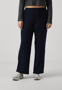 Navy ribbed wide-leg pants made of soft fabric with an elastic waistband, paired with light-colored athletic shoes.