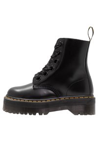 Botín negro de tobillo hecho de cuero brillante con una suela gruesa y transparente, con costuras amarillas, punta redonda y diseño con cordones.