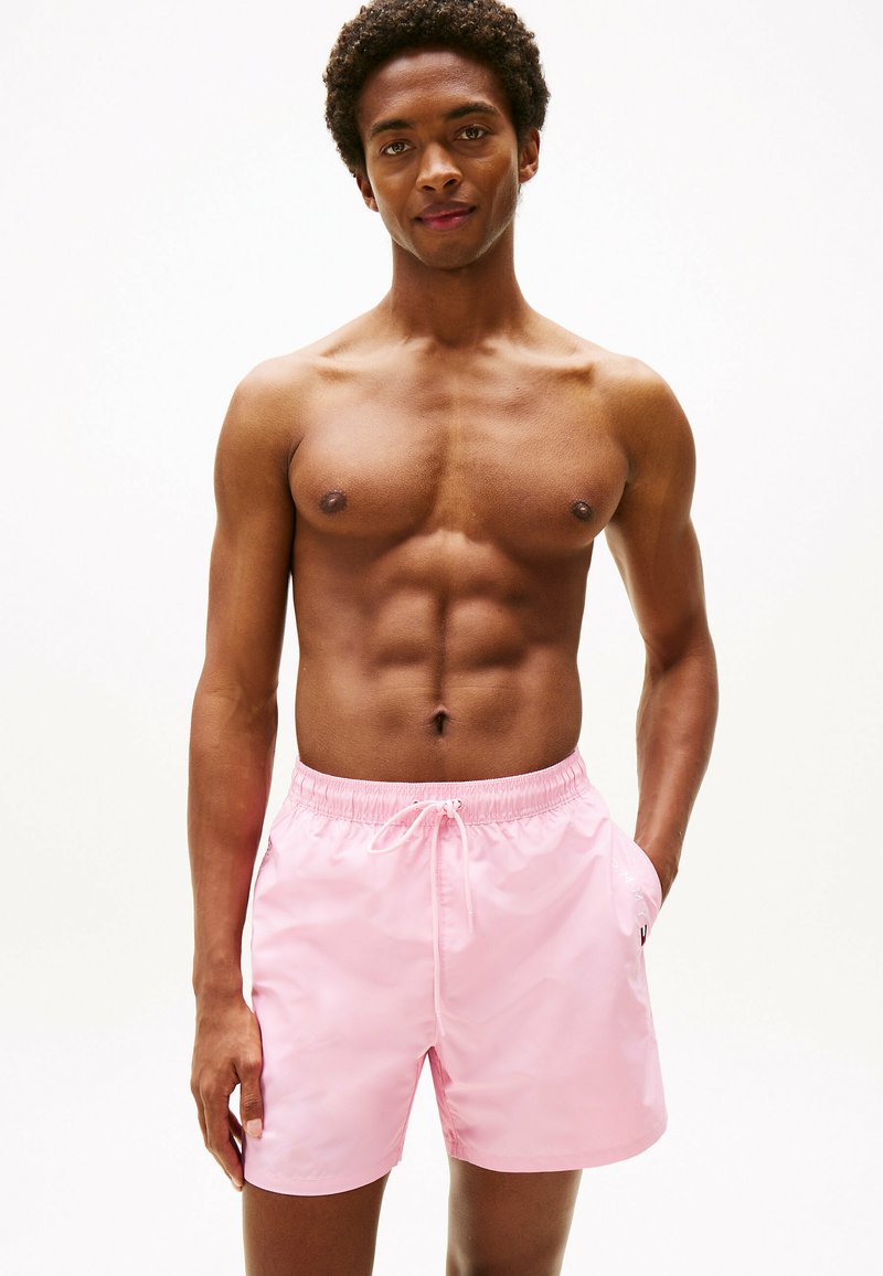Pantaloni da nuoto rosa realizzati in tessuto leggero, con cintura elastica e coulisse. Presentano tasche laterali e una superficie liscia.