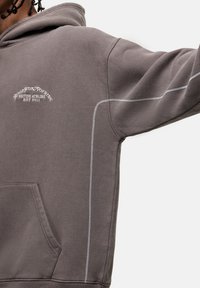 Felpa grigia con dettagli di cucitura bianchi, tasca frontale e logo ricamato sul petto. Tessuto morbido e vestibilità casual.