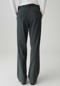 Dunkelgrüne, weit geschnittene Hose aus glattem Material, mit elastischem Bund und zwei Gesäßtaschen mit Knopfverschluss.