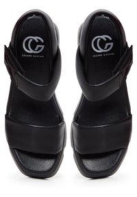 Paire de sandales noires à bouts ouverts avec des larges brides et une fermeture Velcro à la cheville, avec le logo Cesare Gaspari à l'intérieur des talons.