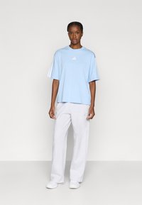 Világoskék rövid ujjú póló fehér logóval, szürke melegítőnadrággal párosítva. A póló lazán illeszkedik; a nadrág bő és egyenes szár�ú.