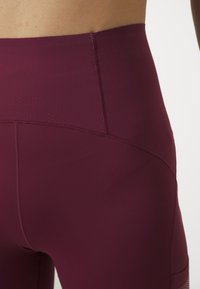 Bordó, magas derekú leggings, texturált, rugalmas anyagból készült, lapos varrásokkal és testhezálló kialakítással, sportolásra alkalmas.