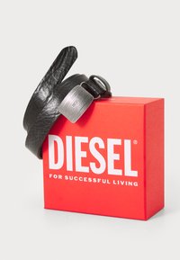 Bracelet en cuir noir avec une finition texturée, doté d'un fermoir en métal portant l'inscription "DIESEL," présenté à côté d'une boîte rouge avec un texte blanc.