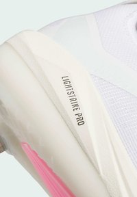 Bijela atletska cipela s teksturiranim dizajnom, laganom konstrukcijom i ružičastim naglascima na potplatu. "LIGHTSTRIKE PRO" otisnuto sa strane.