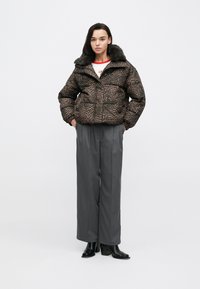 Rjavi puhasti plašč z vzorcem leopardove kože in ovratnikom iz umetnega krzna, kombiniran s sivimi širokimi hlačami in črnimi škornji s peto. Gladek, podložen tekstura.