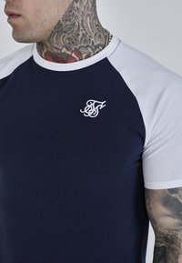 Námornícka a biela tričko s krátkym rukávom vyrobené z bavlny, s okrúhlym výstrihom a malým bielym vyšívaným logom na hrudi.