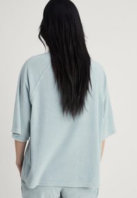 Felpa in pile azzurro chiaro con vestibilità rilassata, maniche a tre quarti e design raglan; texture morbida; senza motivi o dettagli visibili.