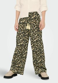 Kalhoty s širokými nohavicemi ve zvířecím vzoru, mají elastický pas a třásňové detaily, vyrobené z lehkého materiálu. Modelka nosí bežové klouzavé boty.