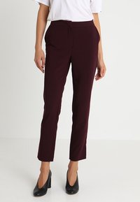 Tyrkysové slim fit kalhoty s hladkou texturou, se bočními kapsami a středním pasem, v kombinaci s černými vysokými podpatky.