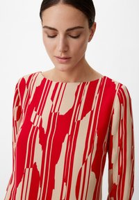 Rotes und beiges Kleid mit einem auffälligen abstrakten Muster, rundem Ausschnitt, langen Ärmeln und einer glatten Stofftextur.