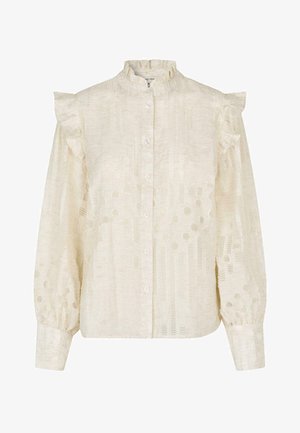 Kreemivärvi bluus, millel on volangiga õlavarre aktsendid, seisev krae, nööbid ees ja tekstuuriga kangas, millel on täppide muster.