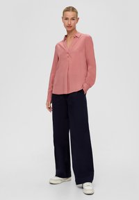 Helles rosa Hemd mit langen Ärmeln, Kragen und lockerer Passform, kombiniert mit weit geschnittenen marineblauen Hosen und weißen Sneakers.