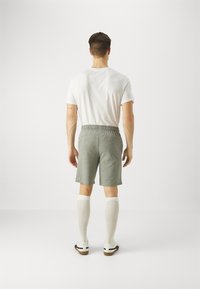 Pantalones cortos de algodón grises con una cinturilla elástica, combinados con calcetines blancos hasta la rodilla y zapatos blancos, vistos desde la parte de atrás.