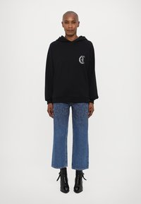 Felpa nera con cappuccio e logo frontale, abbinata a jeans blu a vita alta e cropped con una finitura leggera e stivali neri alla caviglia.
