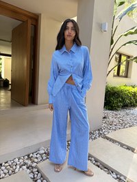 Camisa de botões azul e branca às riscas, com mangas longas, combinada com calças largas. Tecido suave e corte descontraído.