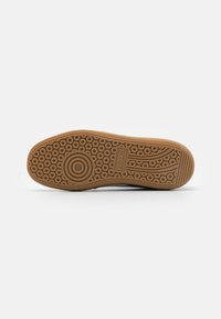 Semelle d'une chaussure Puma marron avec des motifs de bande circulaires et rayés et le logo Puma embossé près du centre.