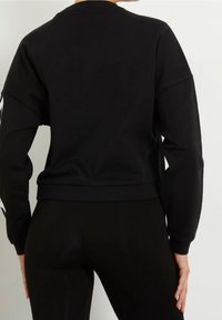 Schwarzer, kurz geschnittener Pullover mit überschnittenen Schultern, weichem Material und geripptem Saum. Ergänzt durch enganliegende schwarze Leggings für einen eleganten Look.