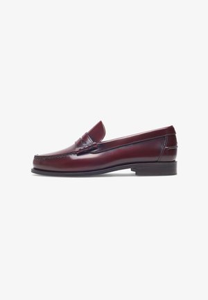 Mocassin en cuir bordeaux avec un bout arrondi, des détails cousus et un petit accent décoratif sur le devant. Semelle plate contrastante.