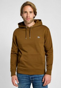 Felpa marrone con cappuccio, cordino, tasca frontale e logo ricamato. Presenta polsini e orlo a coste; abbinata a jeans blu.