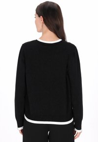 Zwarte gebreide trui met een gestructureerd patroon, voorzien van een contrasterende witte geribbelde halslijn en manchetten. Lange mouwen en een ontspannen pasvorm.
