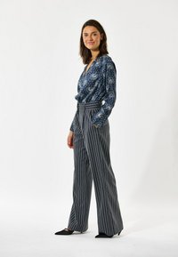 Cvečni temno modri bluzon z dolgimi rokavi, v kombinaciji s širokimi sivo progastimi hlačami in črnimi koničastimi balerinkami. Gladek material in natančna obloga.