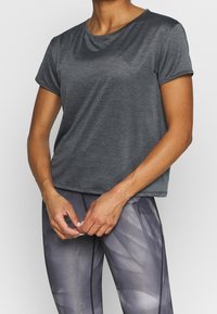 Grå idrottströja med korta ärmar, mjuk textur, rund halsringning och avslappnad passform, kombinerad med mönstrade, ljusgrå leggings.