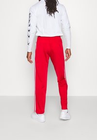 Röda träningsbyxor med vita sidostråk, elastisk midja och en bakficka. Tillverkade av ett slätt, lätt tyg som är idealiskt för sport.