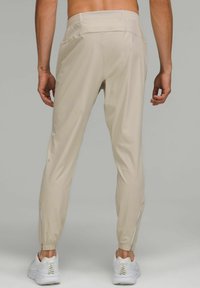 Beige atletiska byxor med elastiska muddar, bakfickor och sidogångjärn. Materialet verkar lätt och slätt, ihop med vita sneakers.