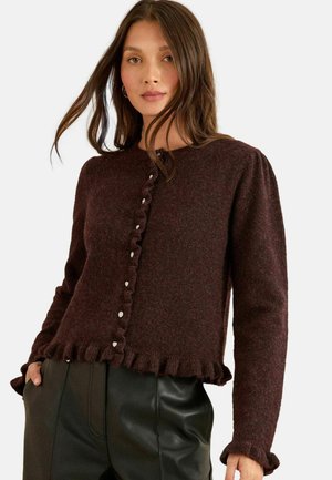 Bordeaux gebreid vest met een ronde halslijn, ruches aan de zoom en zilveren knoopdetails, gecombineerd met zwarte nep leren broek.