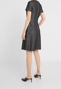 Czarna sukienka z brokatem, z krótkimi rękawami, w kształcie litery A, z zamkiem z tyłu i błyszczącą teksturą. Połączona z czarnymi klapkami na obcasie.