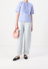 Haut à manches courtes rayé bleu et blanc avec un devant volanté, associé à un jean large bleu clair et des ballerines noires avec des détails ajourés. Tenue d'un sac rose.